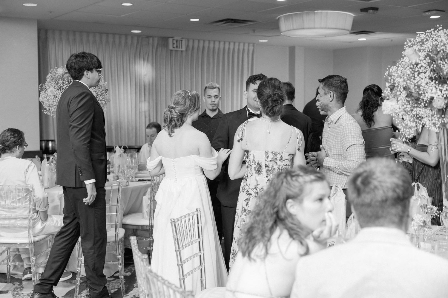 Black and white photo of wedding reception guests mingling and dancing.