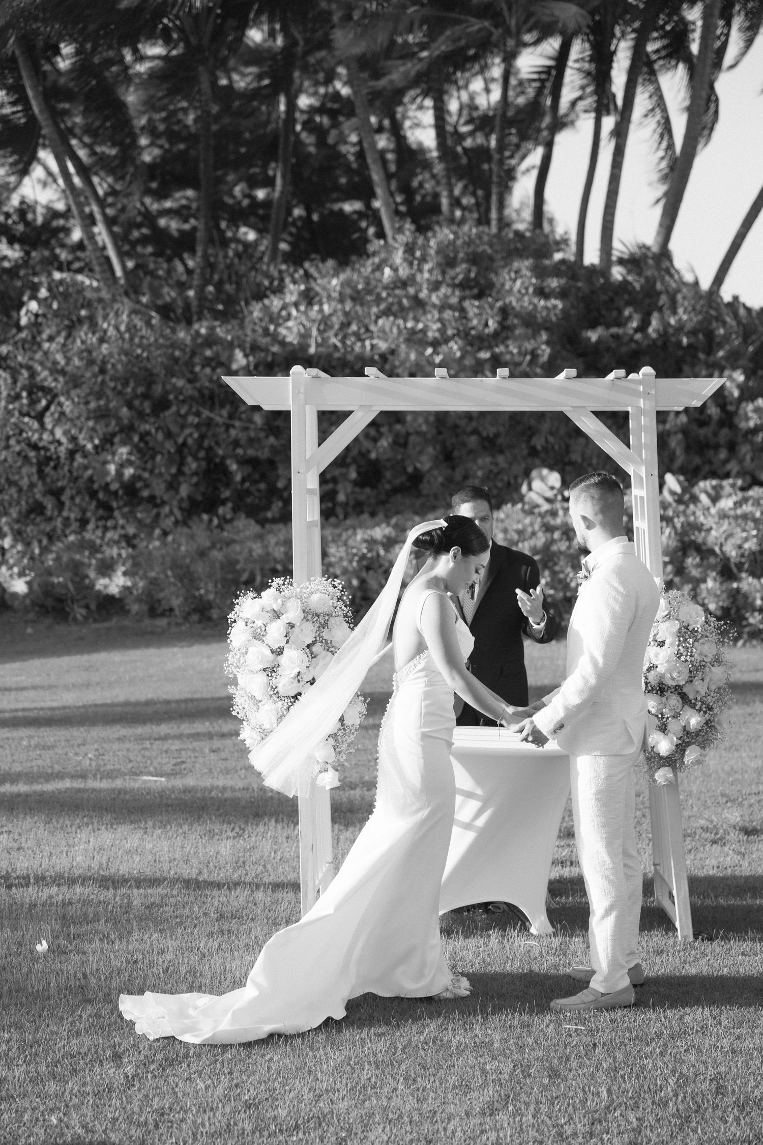 Black and white photo of wedding ceremony under decorated pergola.