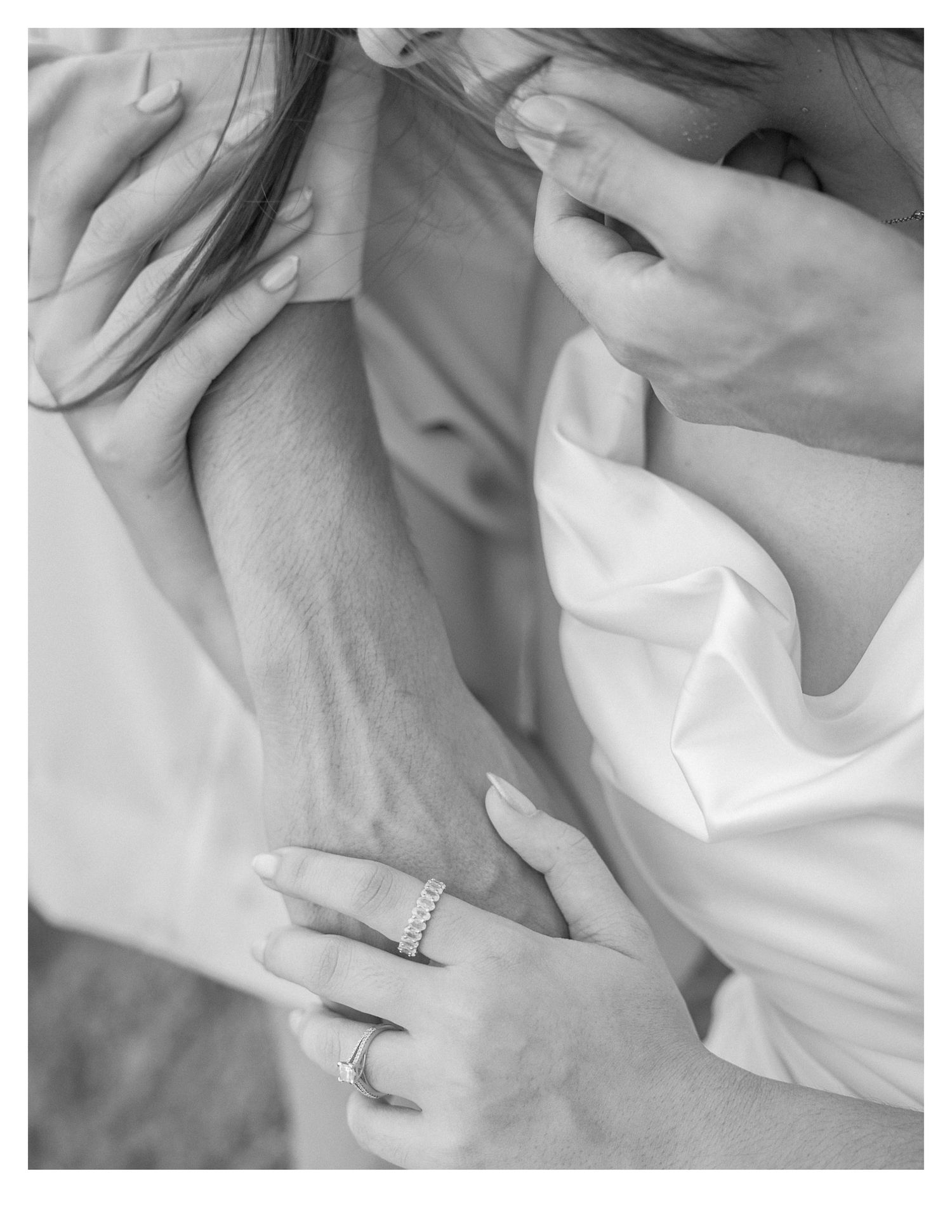 Close-up black and white photo of hands with wedding rings against white fabric.