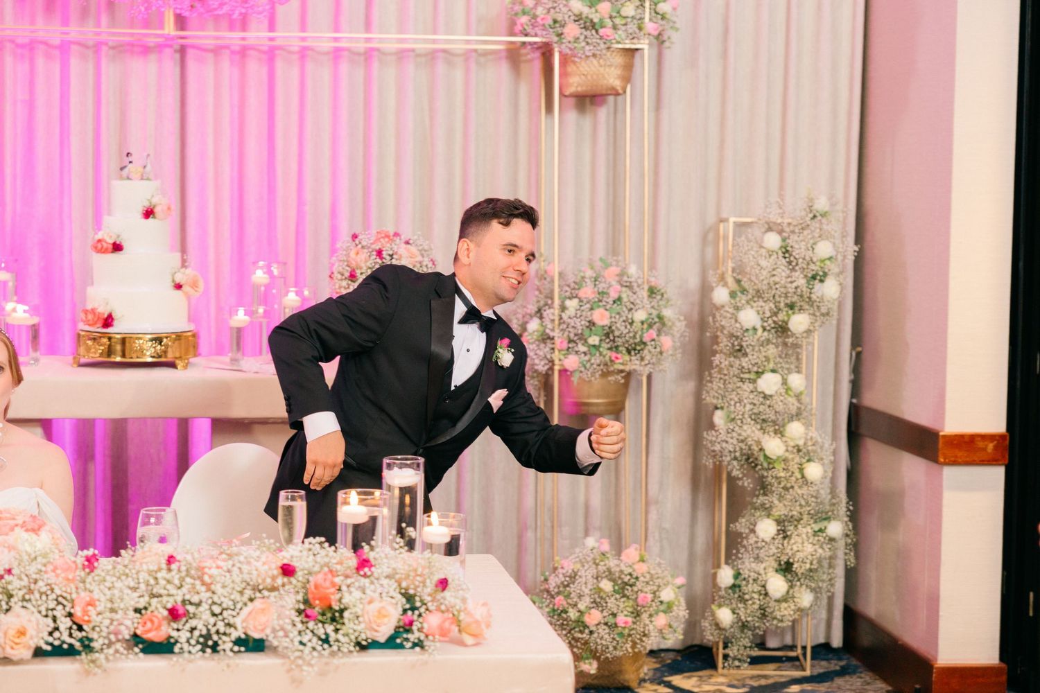 Groom in tuxedo striking playful pose at wedding reception.