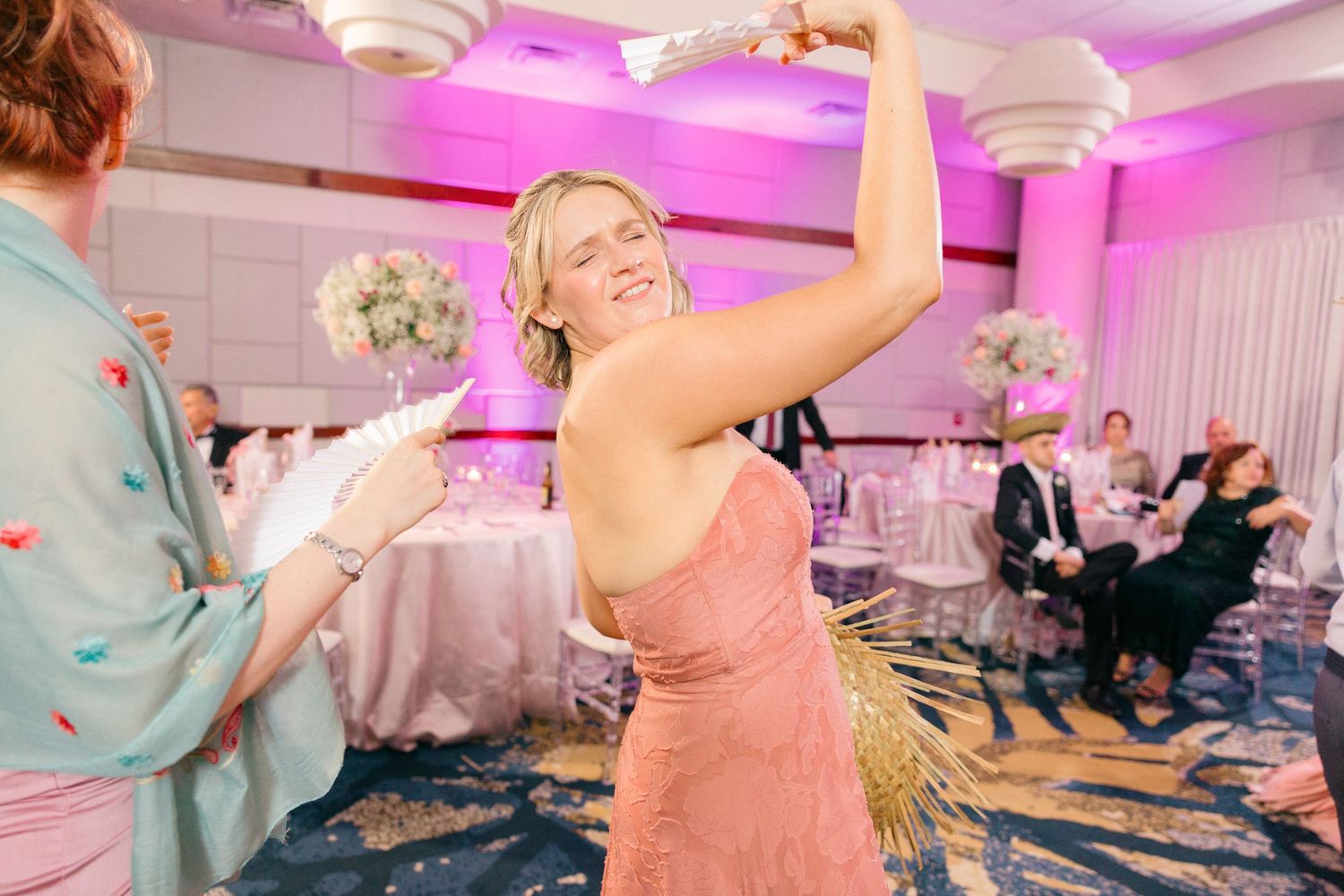 Wedding reception dance floor illuminated with pink lighting as guests celebrate.