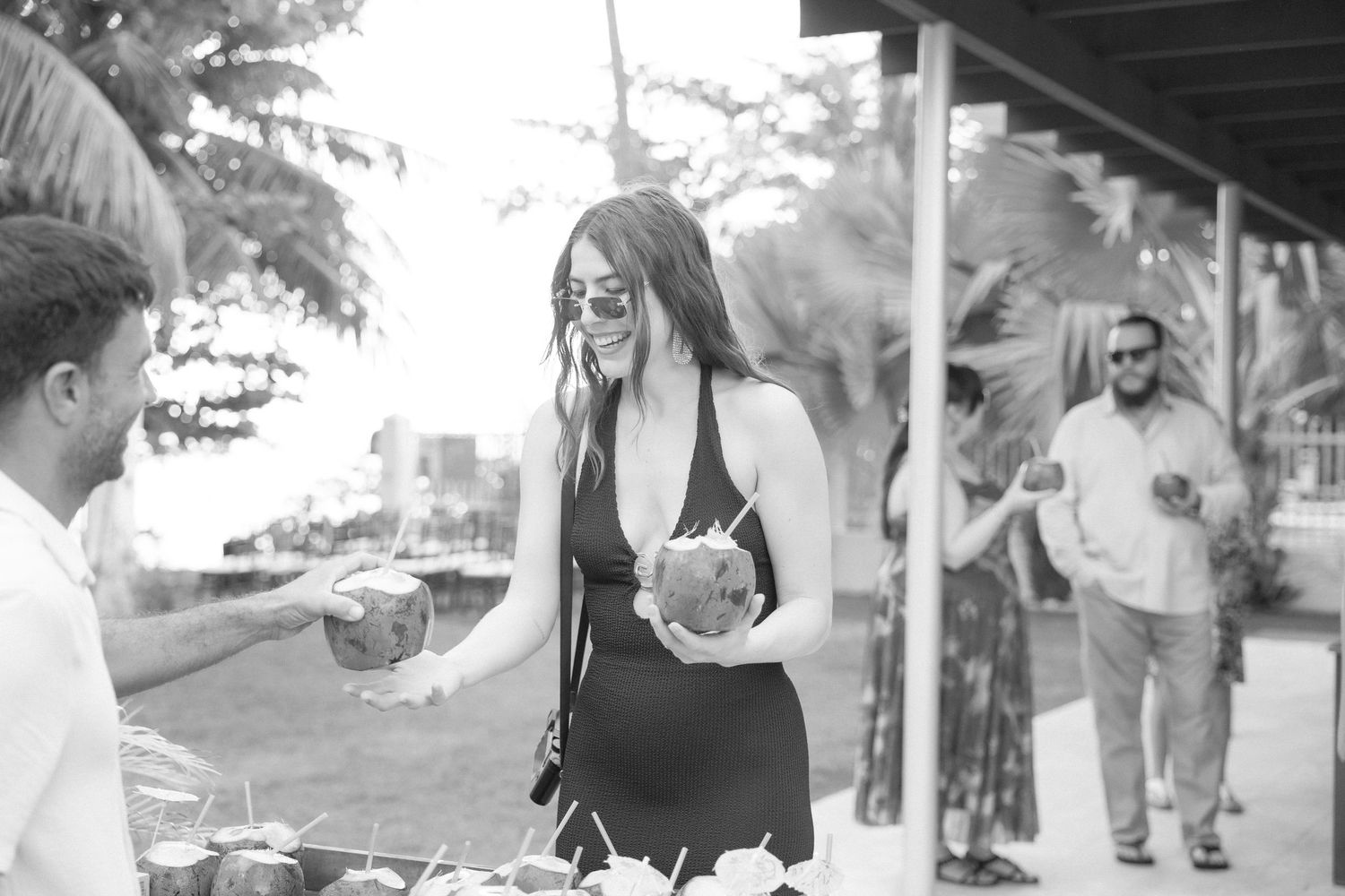 A black and white photo of someone holding a tropical drink at an outdoor venue.