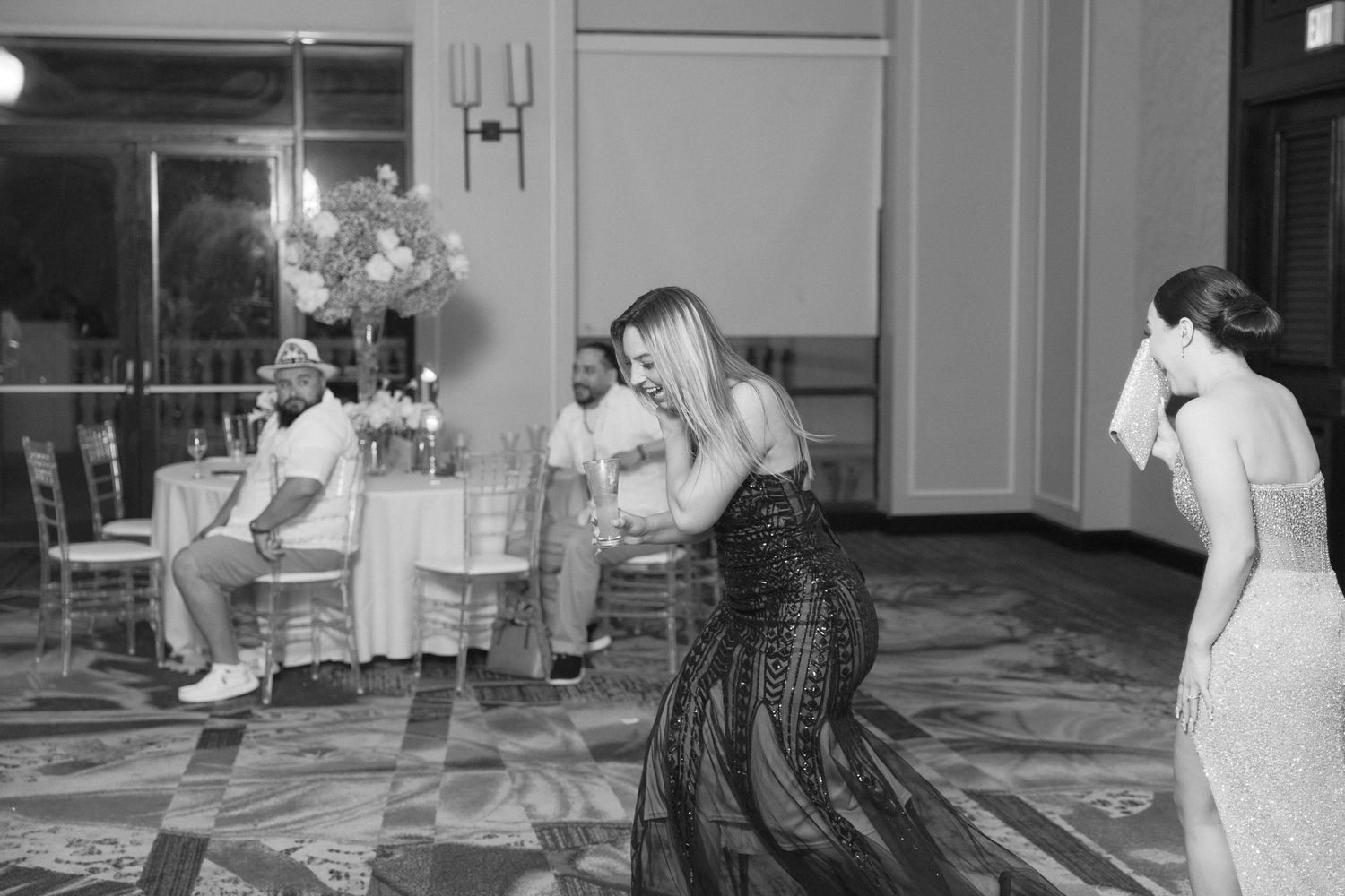 Black and white photo of guests dancing in formation at a wedding reception.