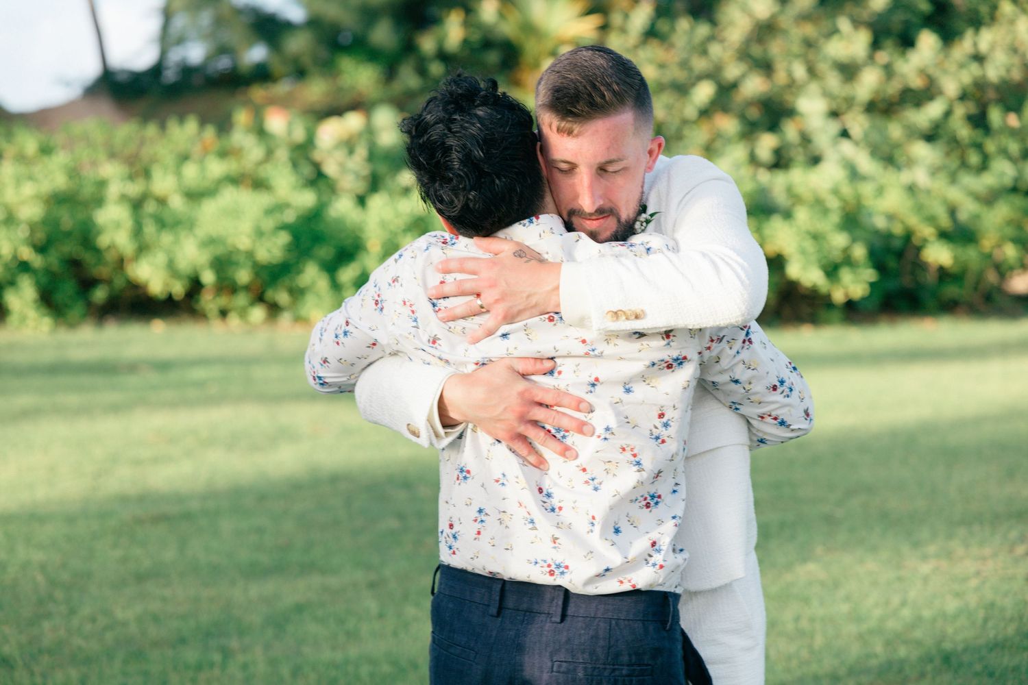 Wedding celebration embraces on a sunny lawn with white attire.