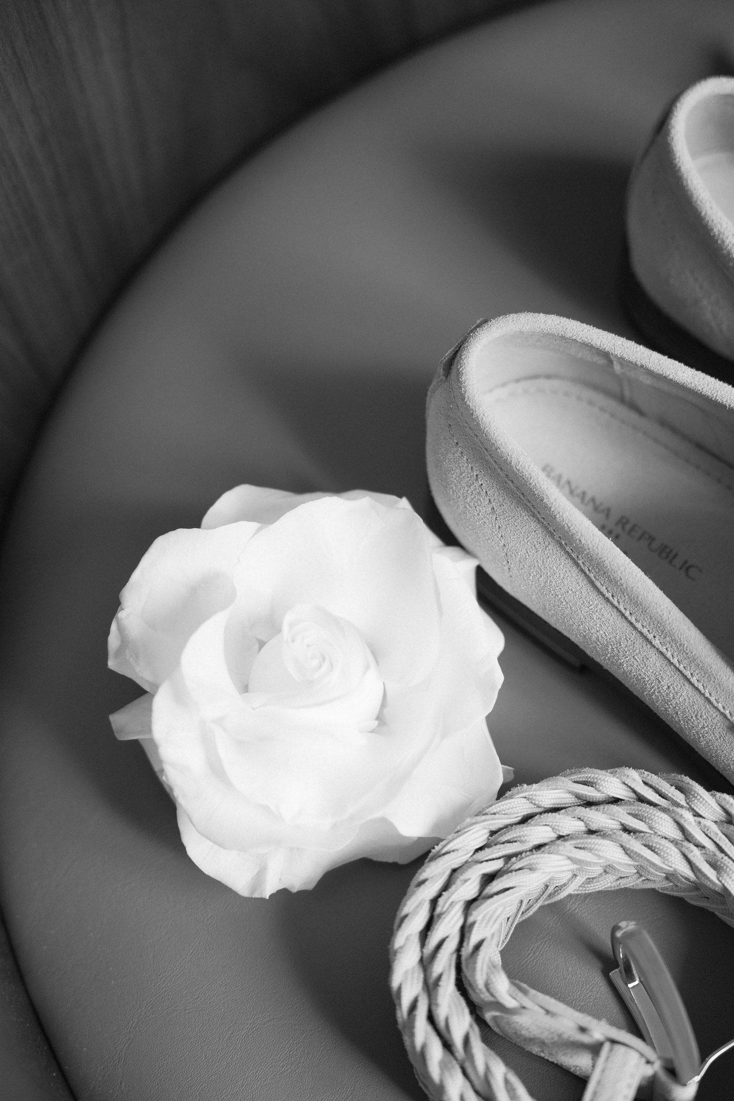 Artistic black and white detail shot of white rose with loafers and braided cord.
