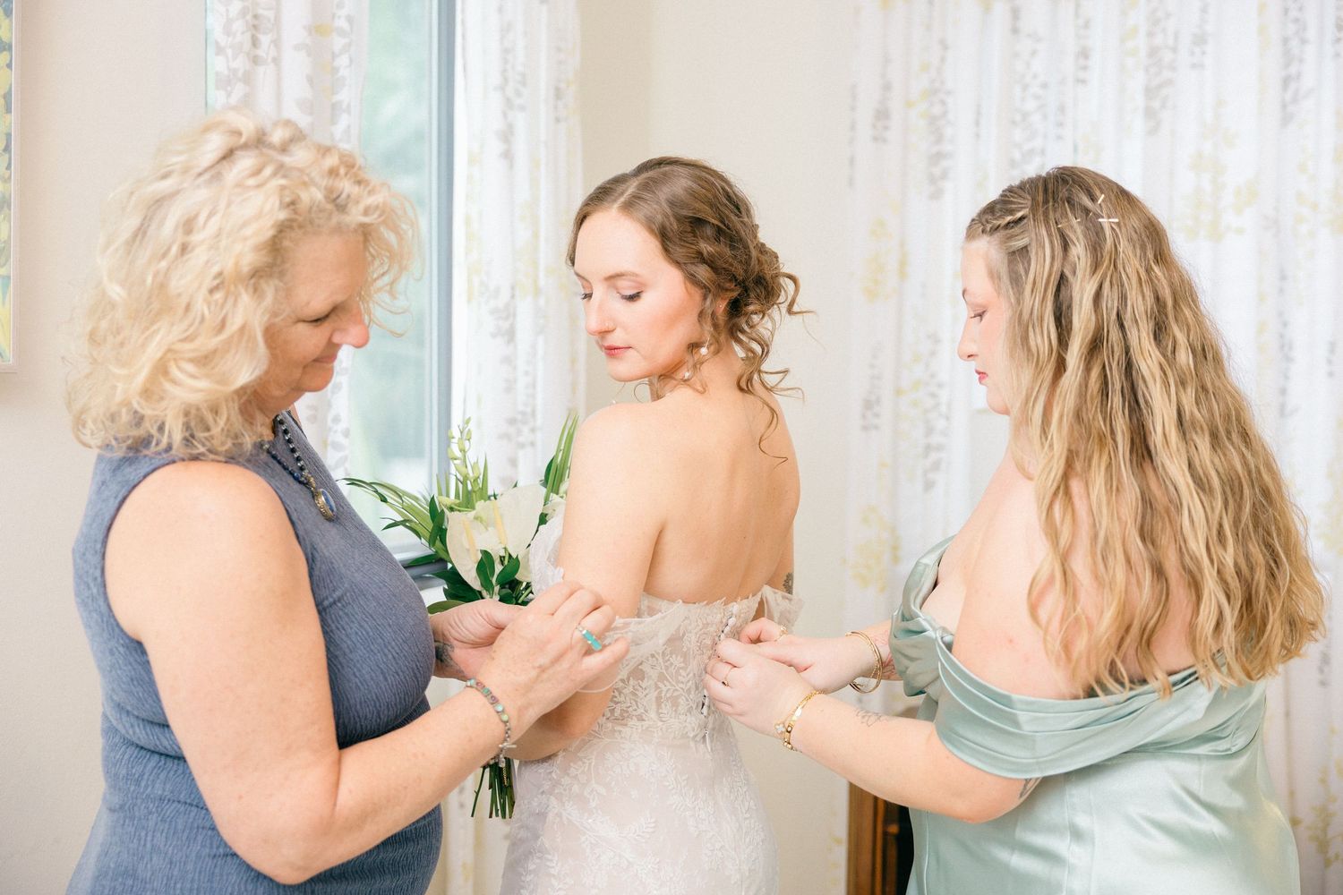 Bridesmaids in blue dresses helping with wedding preparations in a bright room.