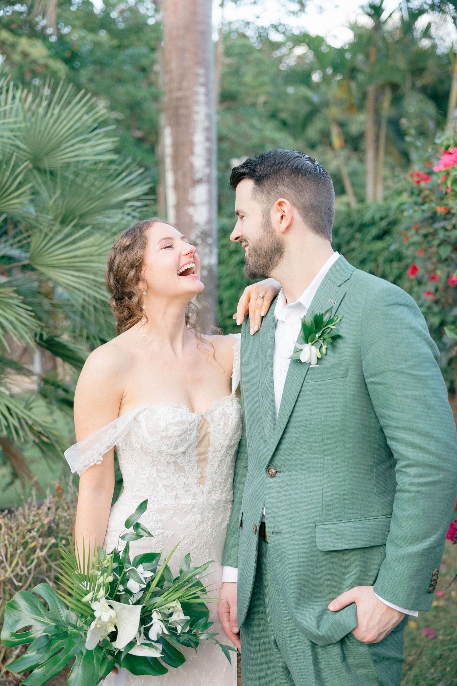 Joyful wedding portraits in a tropical garden with palm trees and bright red flowers.
