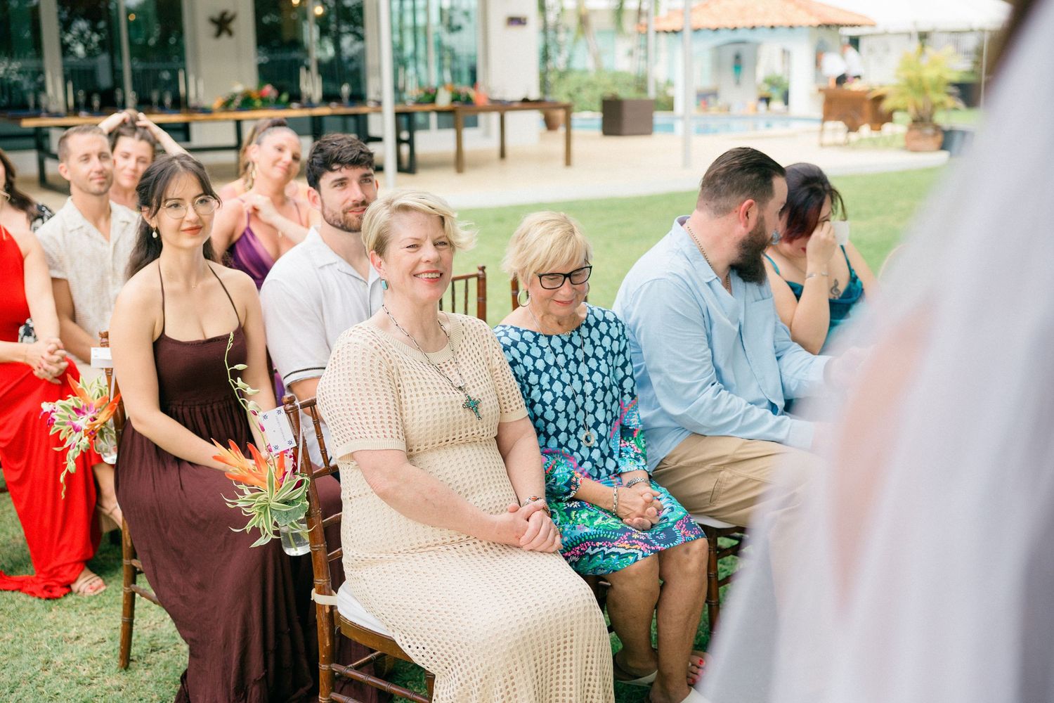 Outdoor wedding reception with guests seated at tables under covered patio.