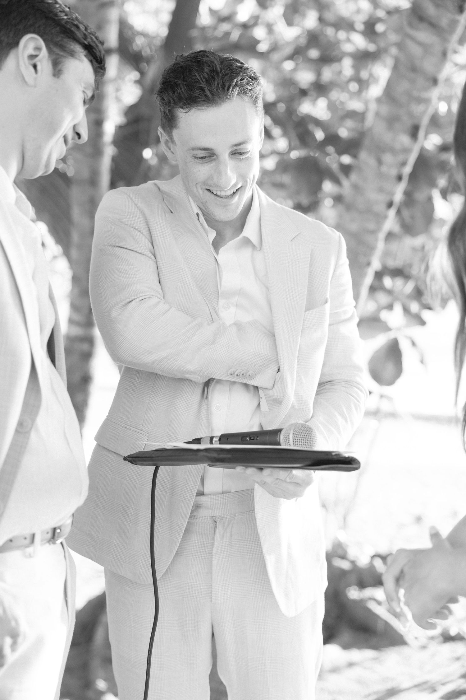 Wedding party members in light colored suits carrying serving trays at an outdoor event.