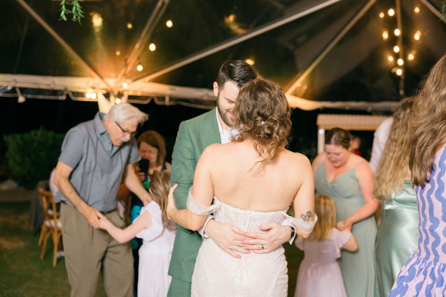 Wedding guests dance together at an outdoor evening reception under string lights.