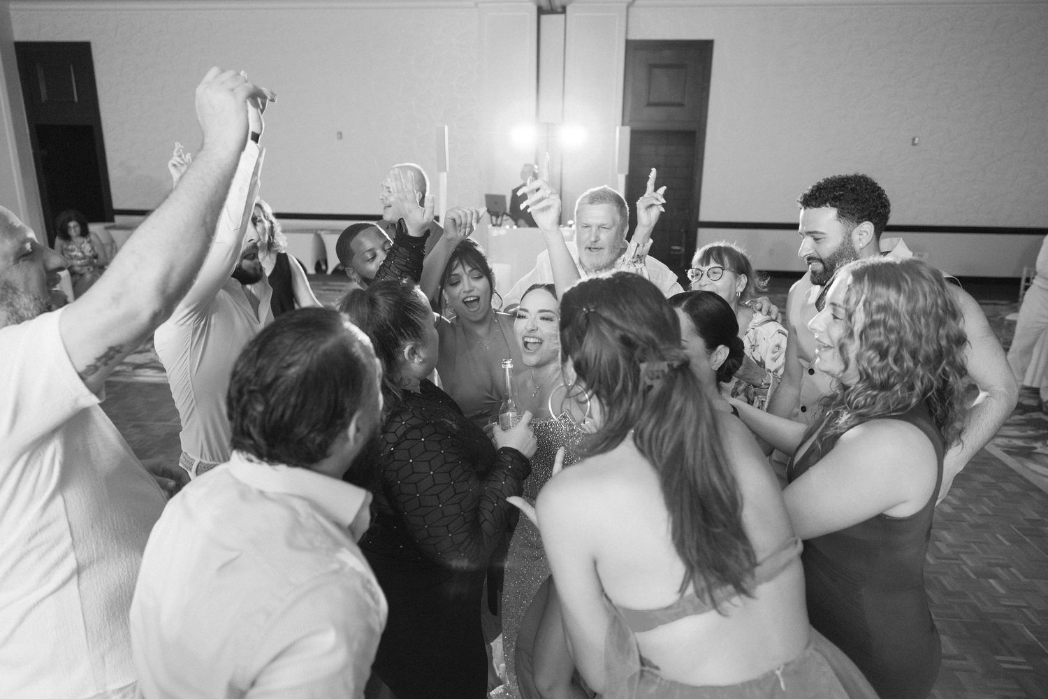 Black and white shot of wedding guests dancing with their arms raised in celebration.