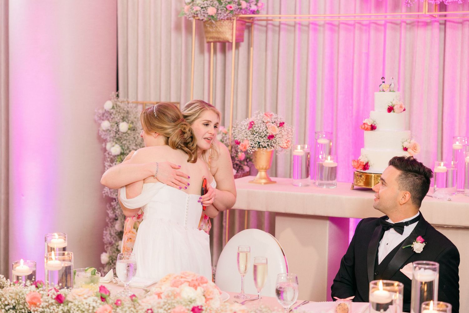 Elegant wedding reception with pink uplighting and white floral arrangements on tables.
