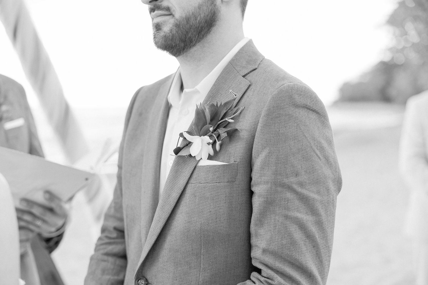 Groom and groomsmen in grey suits standing together at beach wedding.