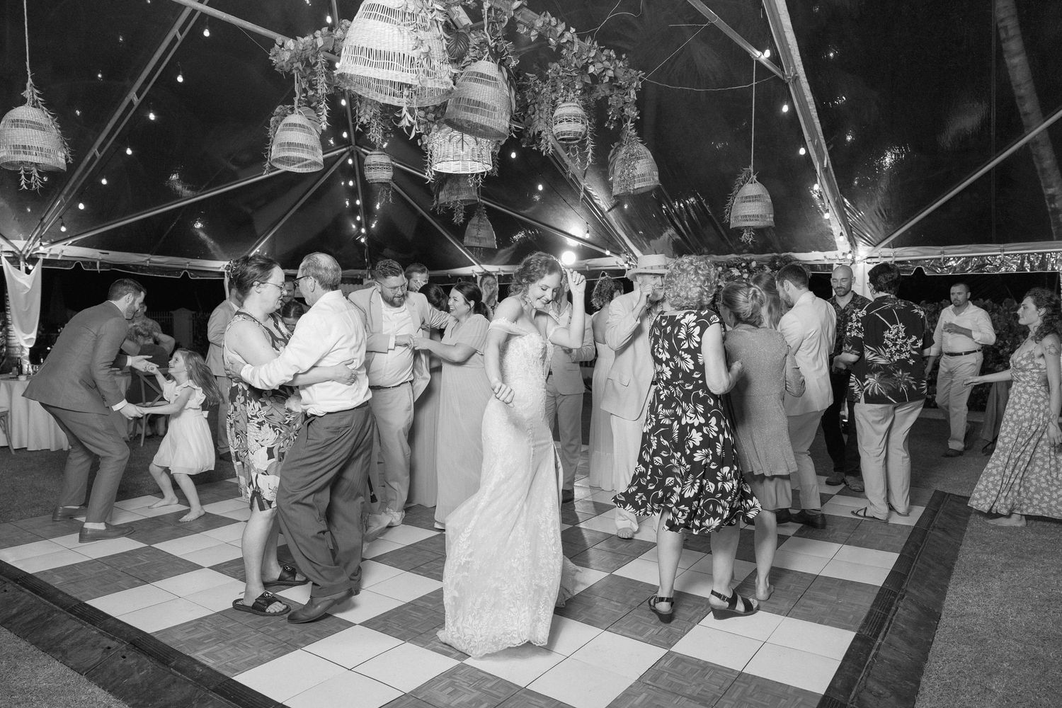 Wedding guests dancing and celebrating on a black and white checkered dance floor under string lights.