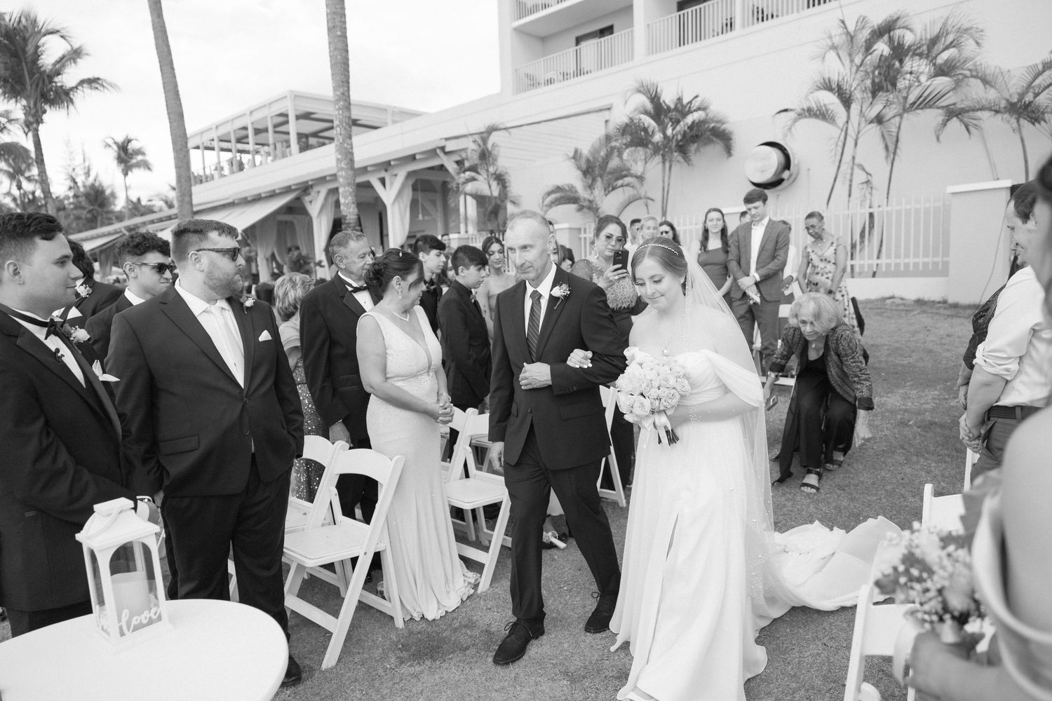 Black and white photo of wedding guests watching ceremony proceedings outdoors.