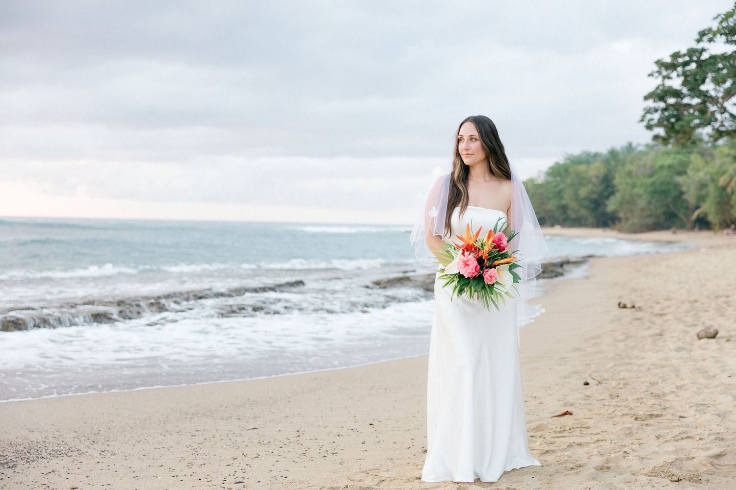 A white dress and tropical bouquet on a scenic beach with ocean waves in the background.