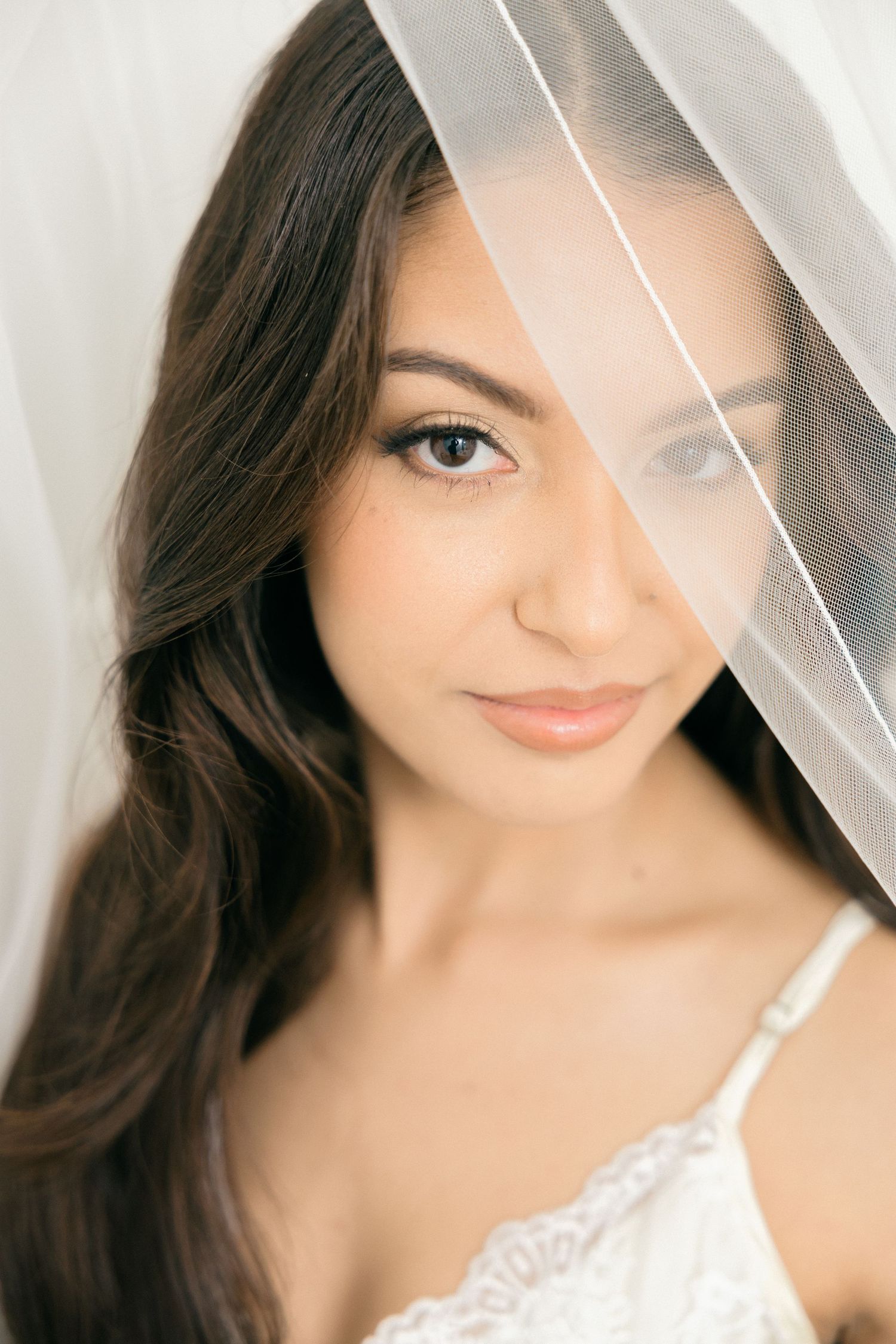 Close-up bridal portrait with soft lighting and sheer veil creating romantic ambiance.