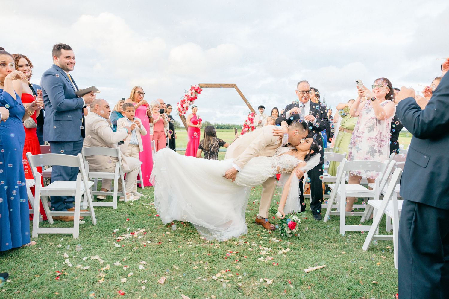 Wedding guests celebrate and throw petals during an outdoor ceremony exit.