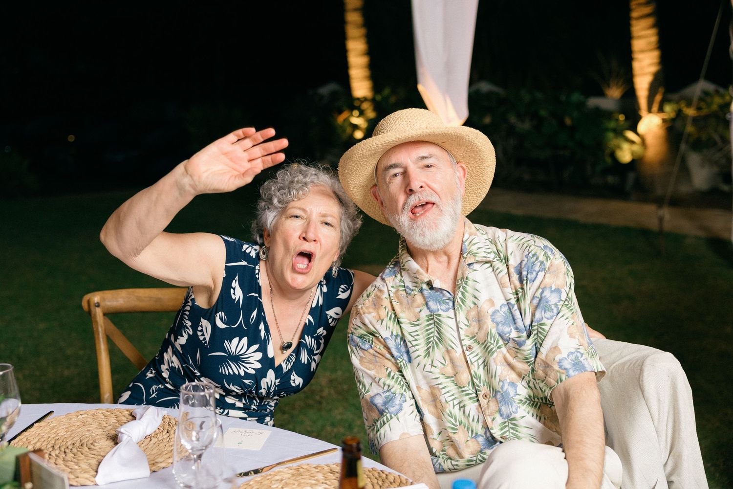 Guests in tropical attire enjoying an outdoor wedding reception with animated expressions.