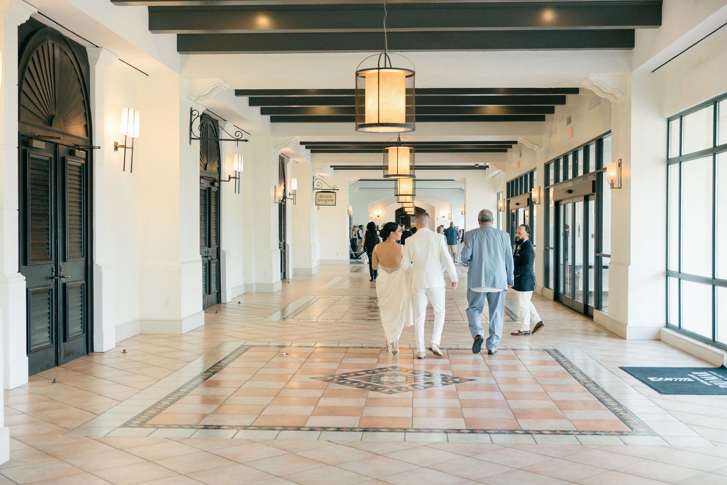 People walking down an elegant hallway with exposed wooden beams and pendant lighting.