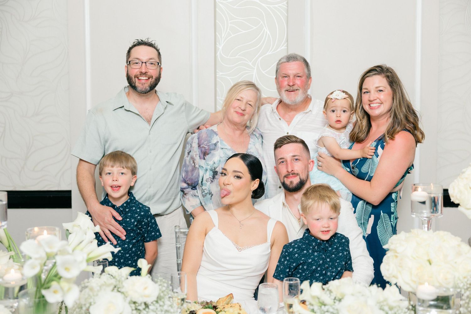Joyful wedding party and family members posing together with white floral decorations.