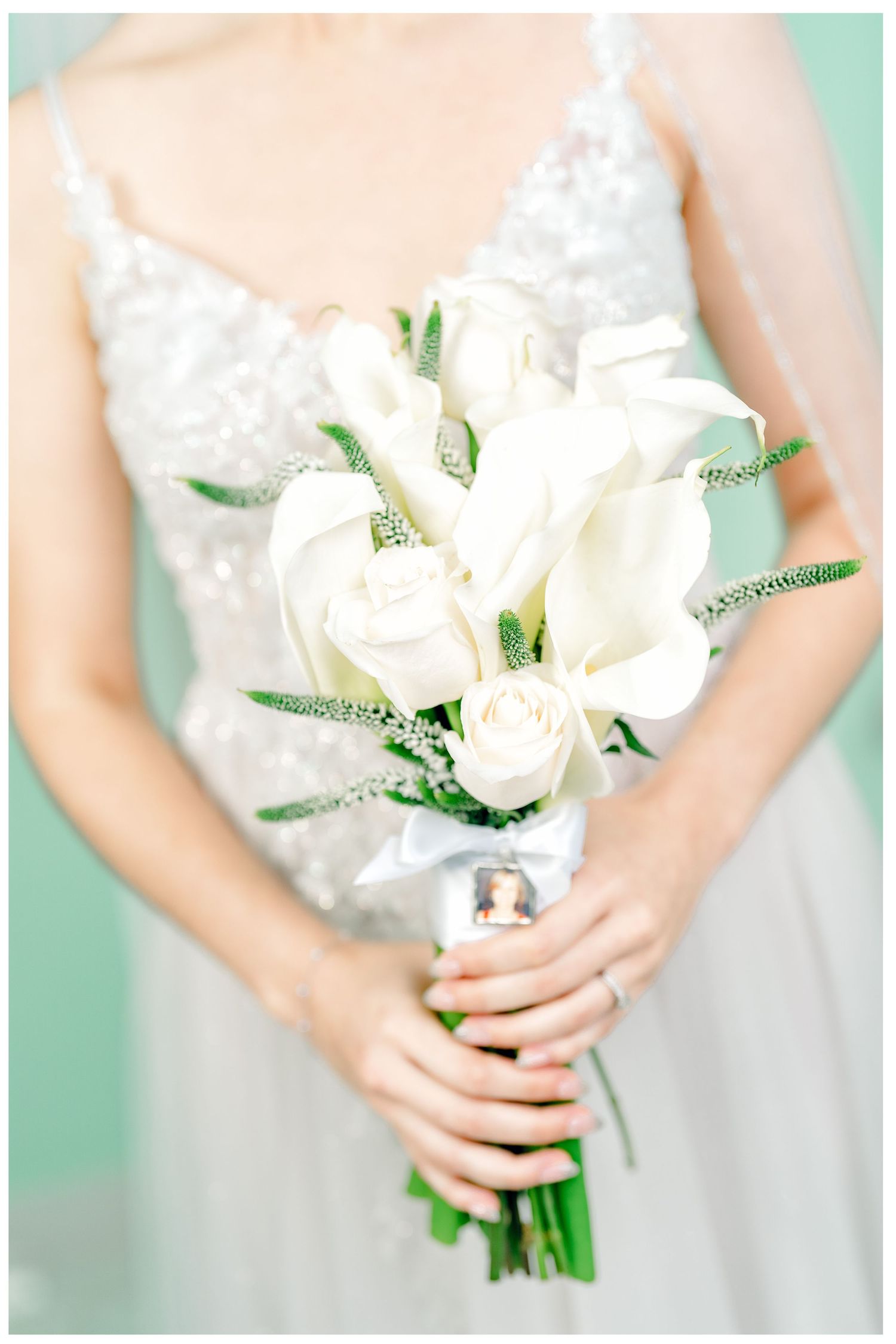 Elegant white rose and calla lily bridal bouquet with greenery against a mint background.