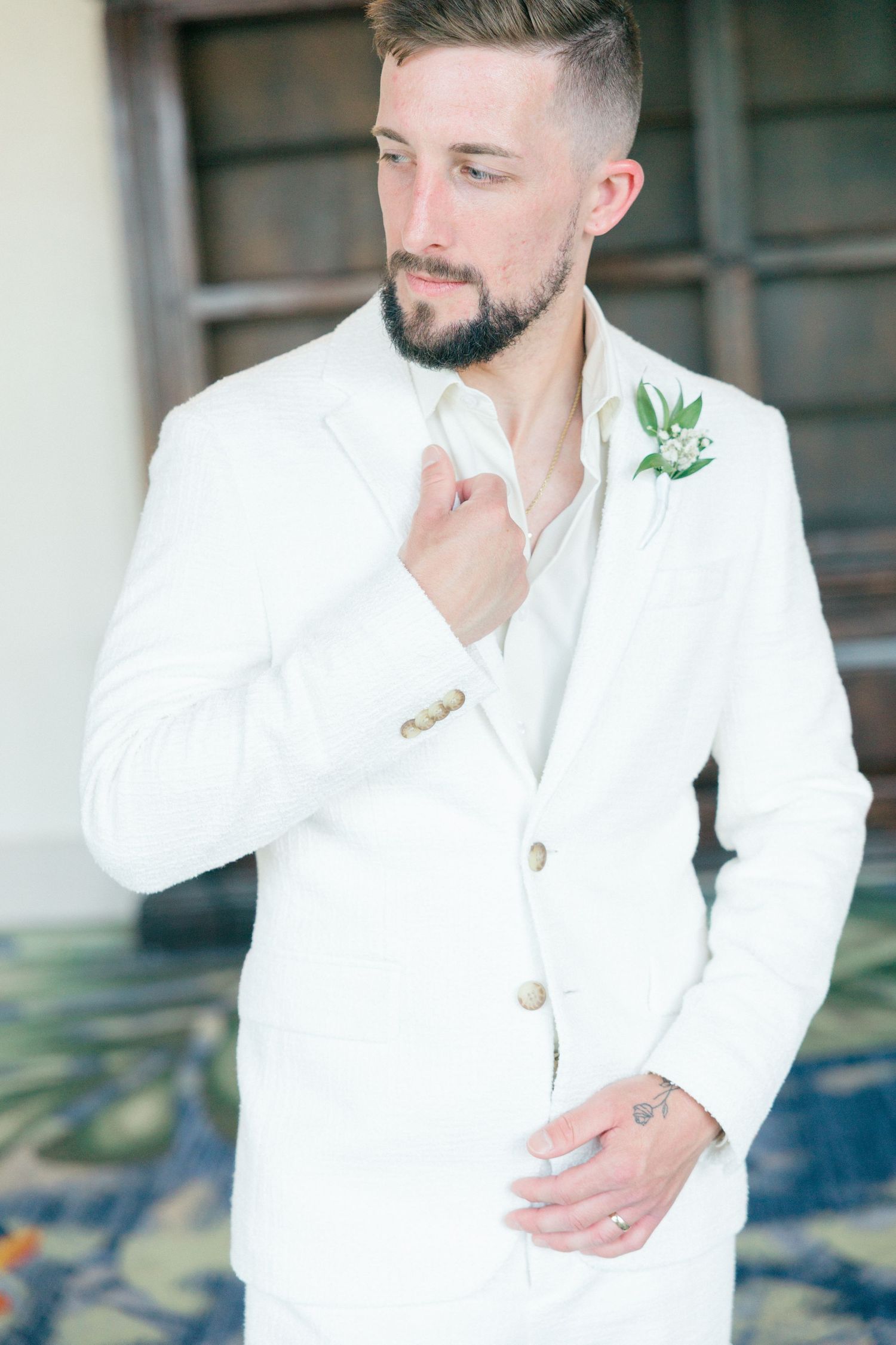 Elegant wedding detail shots showing a groom in white attire with boutonniere against a modern interior backdrop.