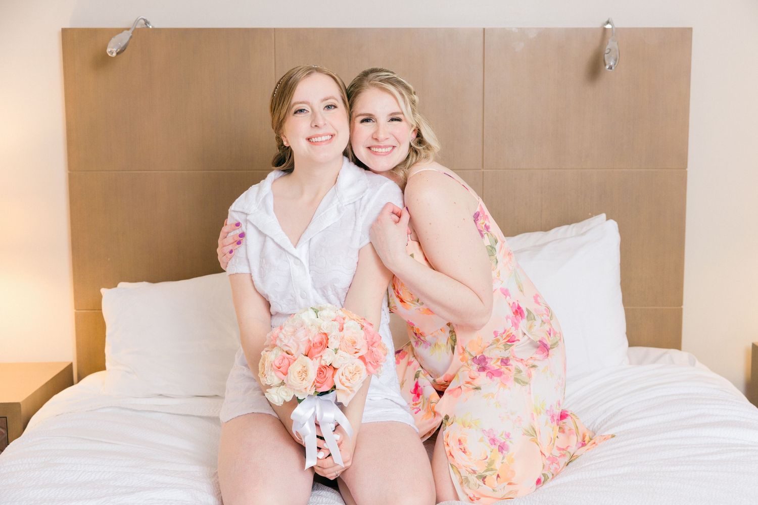 Group in pink and coral dresses sitting together on a white bed.