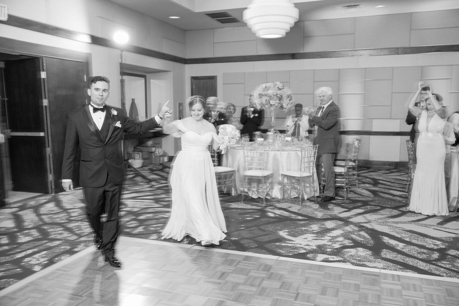 A couple shares their first dance at a wedding reception in a ballroom with guests watching from the sides.