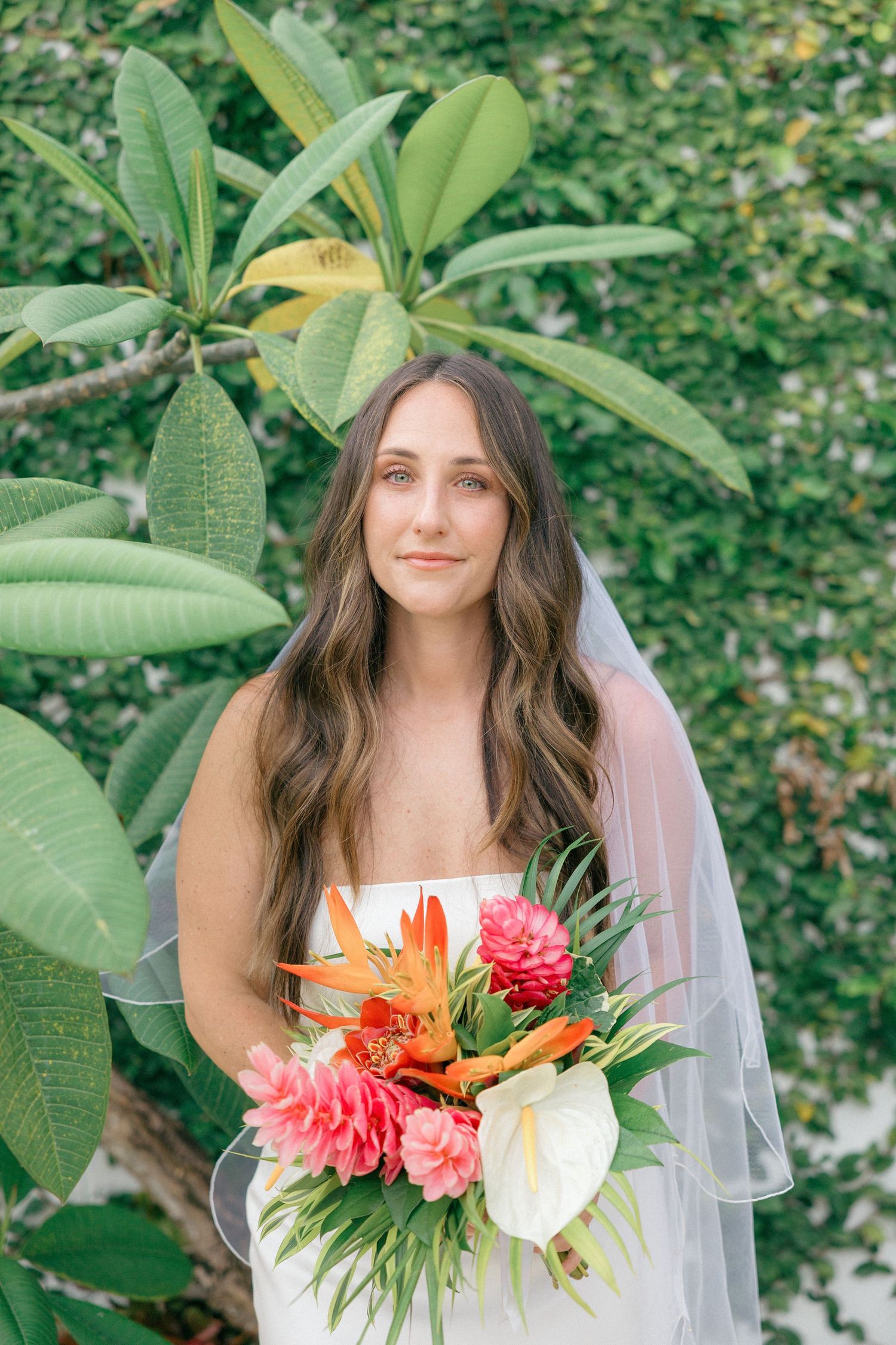 Bridal portrait with tropical flowers against lush green foliage background.