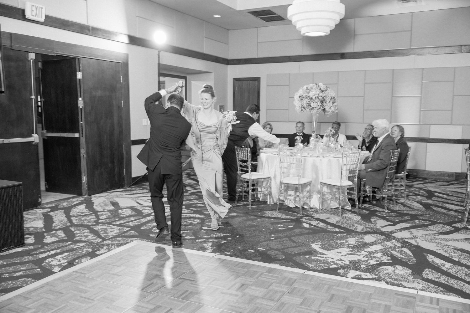 Wedding reception scene with guests seated at tables while couple dances.
