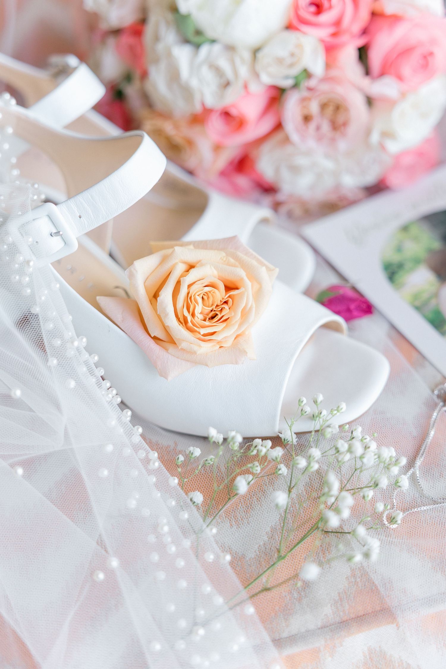 Wedding details featuring white heels, roses, and delicate baby's breath on soft tulle.