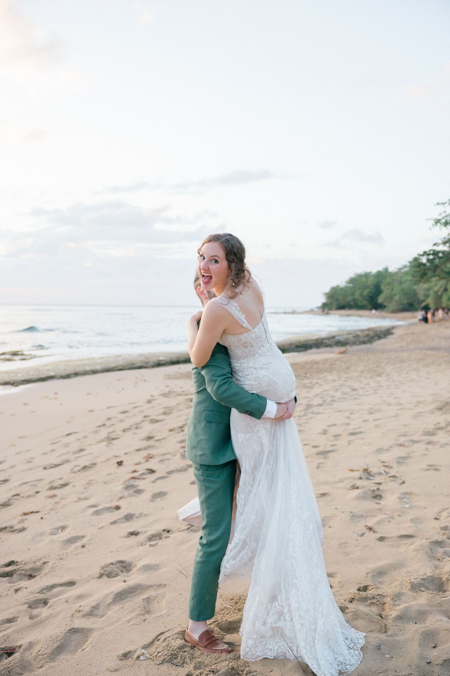 Joyful wedding couple embracing on a sandy beach with ocean waves in the background.