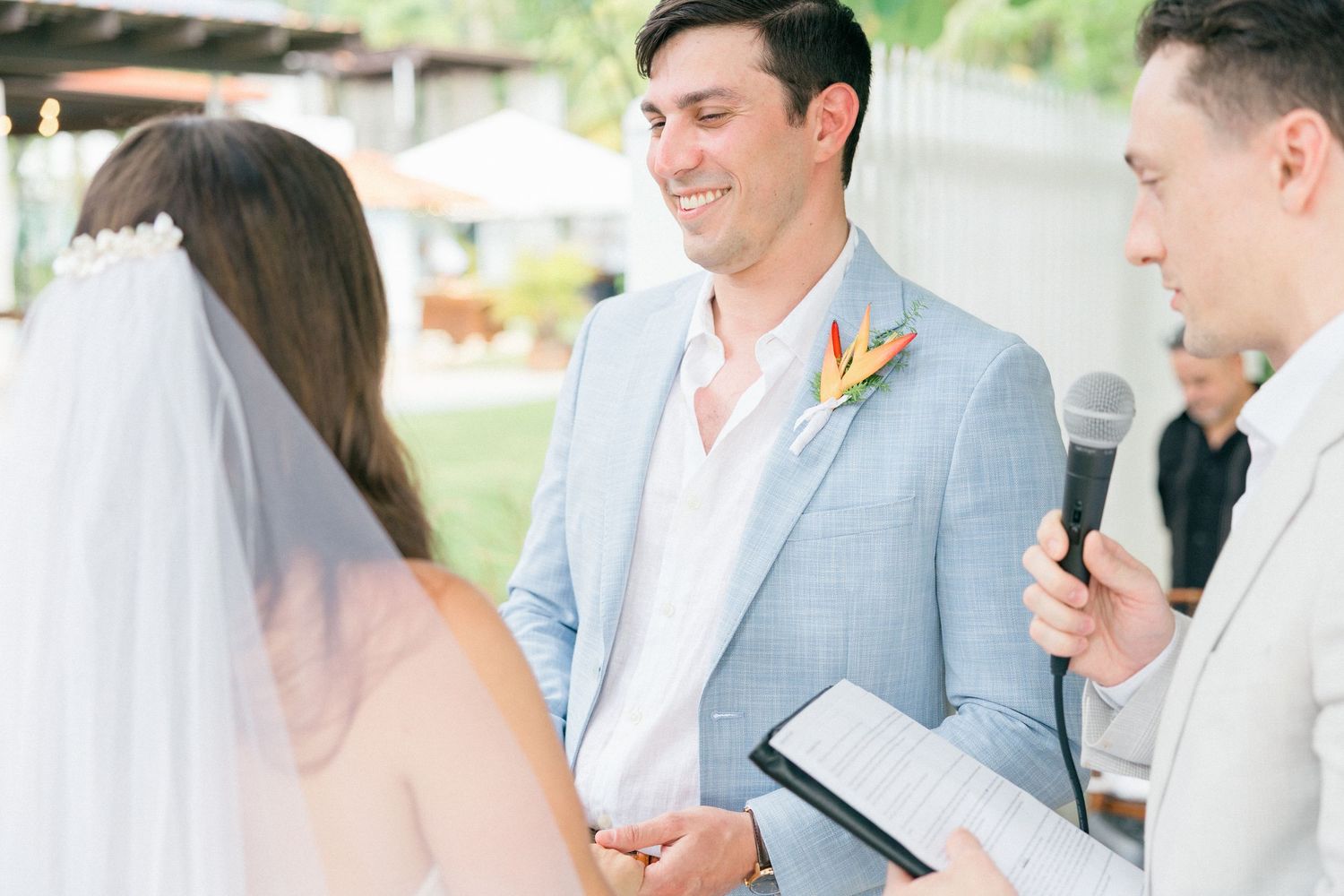 Couple exchanges vows during intimate outdoor wedding ceremony with officiant holding microphone.