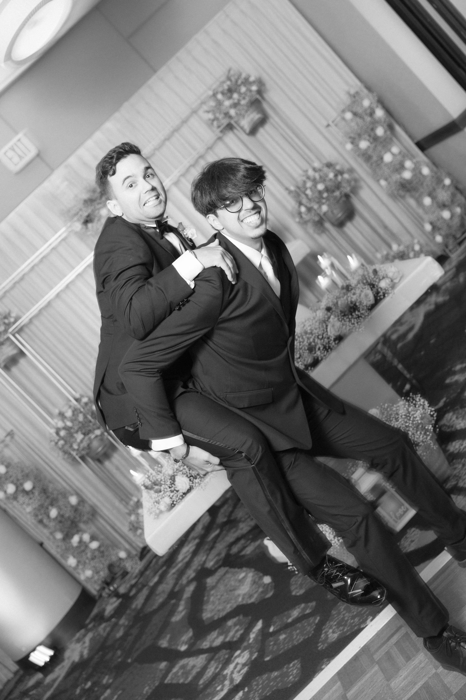 Two people in black suits strike a dramatic pose during wedding celebrations.
