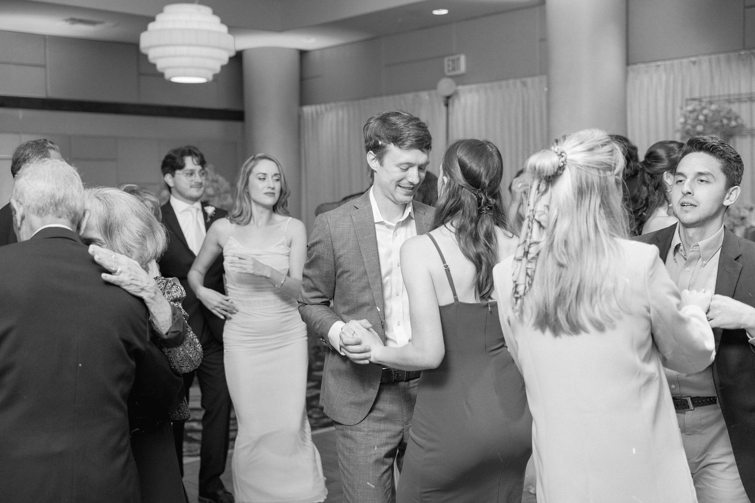 Black and white photo of wedding guests mingling and dancing at the reception.
