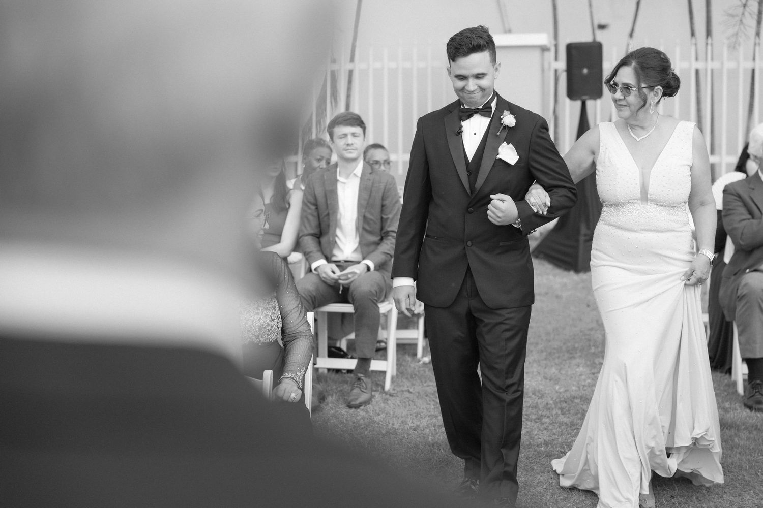 Black and white photo of a wedding processional on a grassy lawn with palm trees.