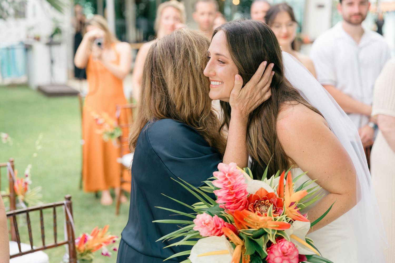 Wedding guests seated at outdoor reception with tropical floral arrangements.