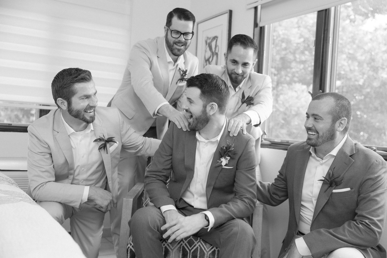 Wedding party members sharing joyful moments and laughter in a sunlit room.