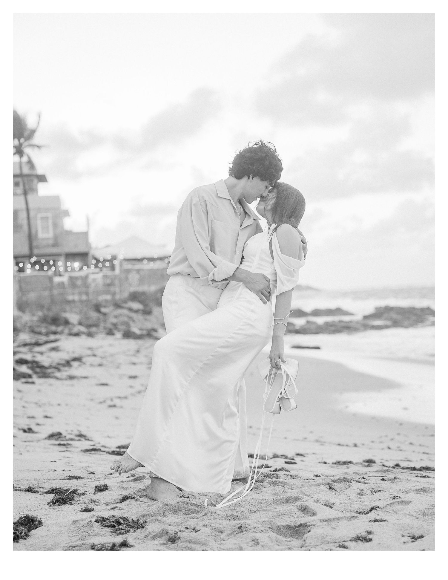 A couple shares an intimate moment on a beach at sunset in black and white.