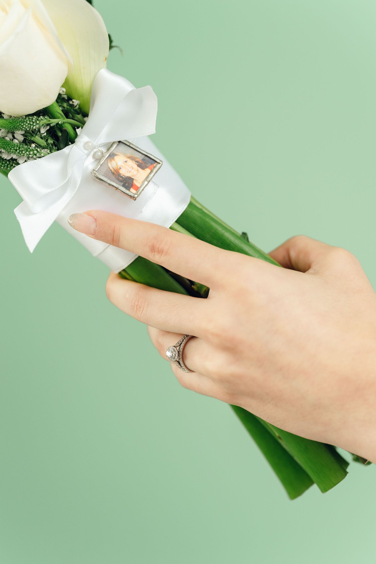 Hand with engagement ring holding green leaves against mint background.