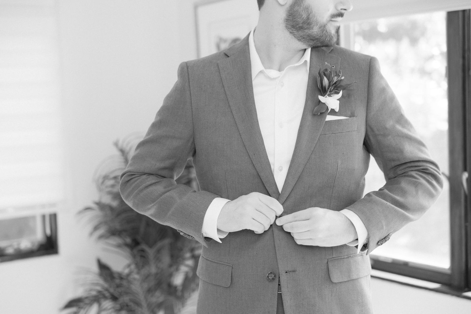 Close-up of groom in gray suit jacket adjusting his buttons before the ceremony.