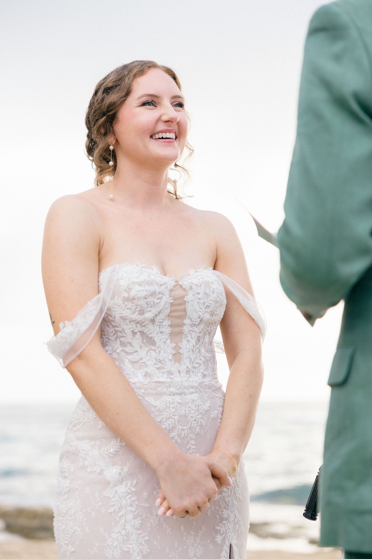 Bride in a detailed lace wedding dress smiles during beach ceremony.