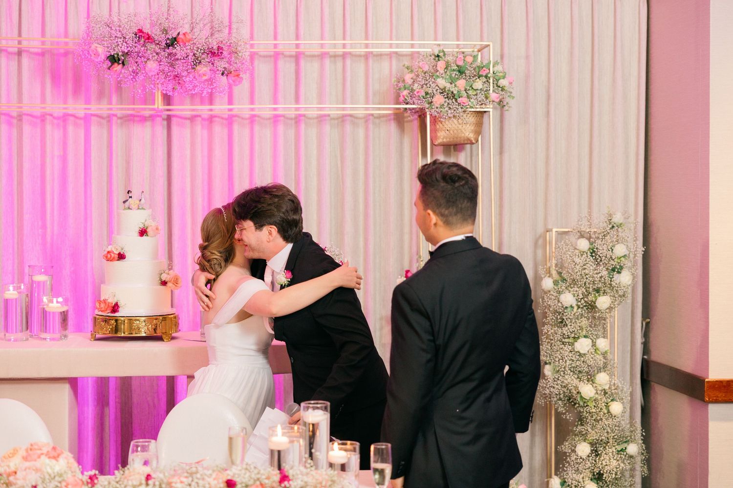 Wedding reception moment with pink lighting and floral decorations.