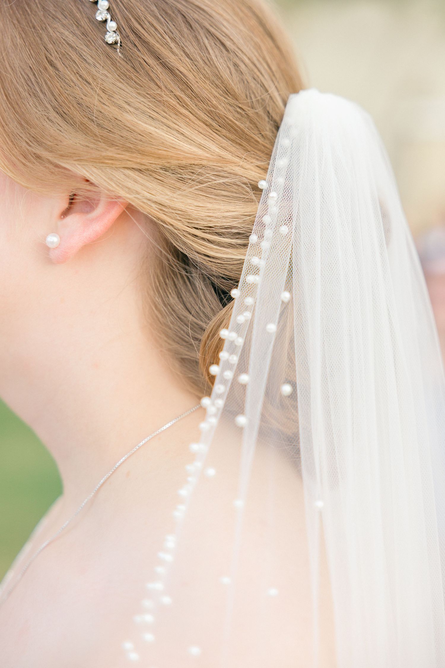 Close-up of delicate pearl-adorned bridal veil against blonde hair.