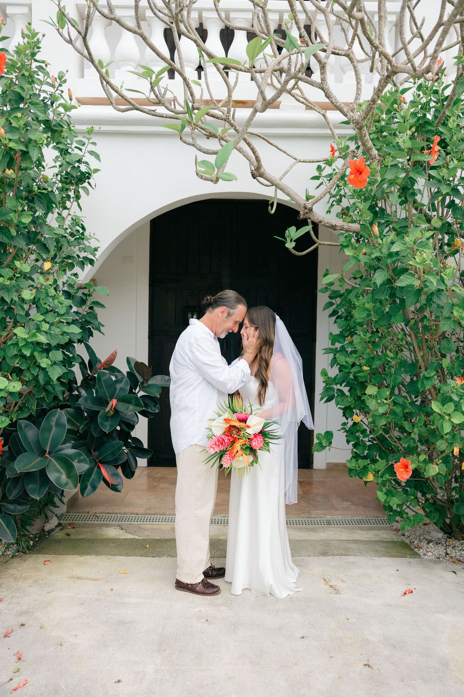 Romantic wedding moment under an arched doorway surrounded by lush tropical foliage.