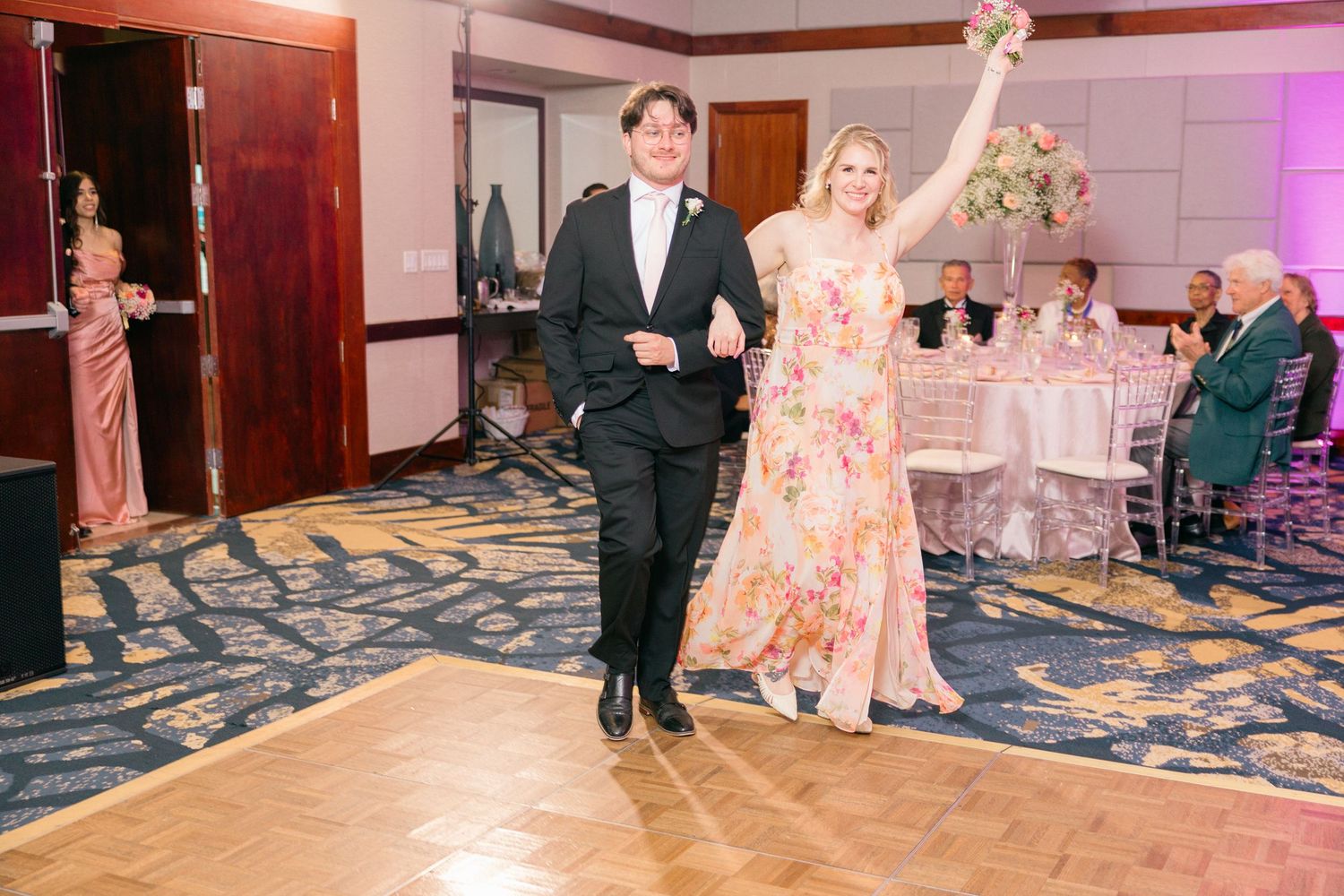 Couple enters reception hall with guests seated at decorated tables.