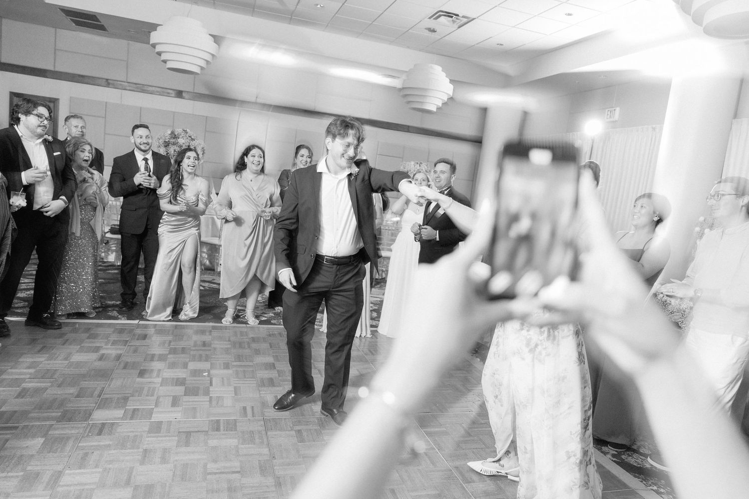 Black and white photo of guests dancing and celebrating at a wedding reception.