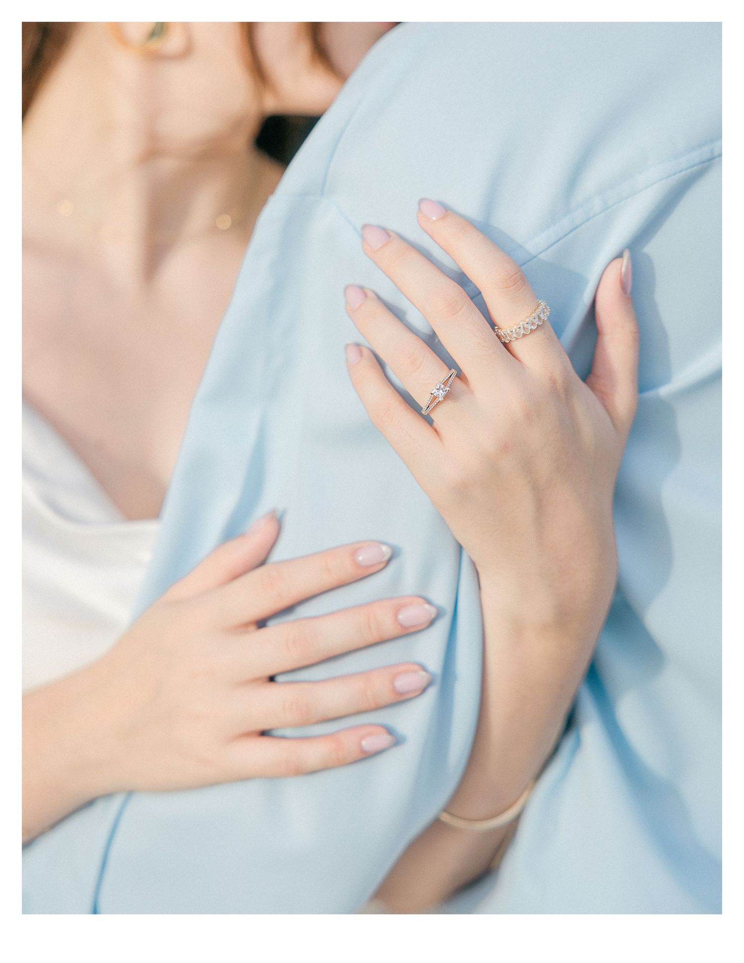 Close-up of hands with engagement ring against light blue clothing.
