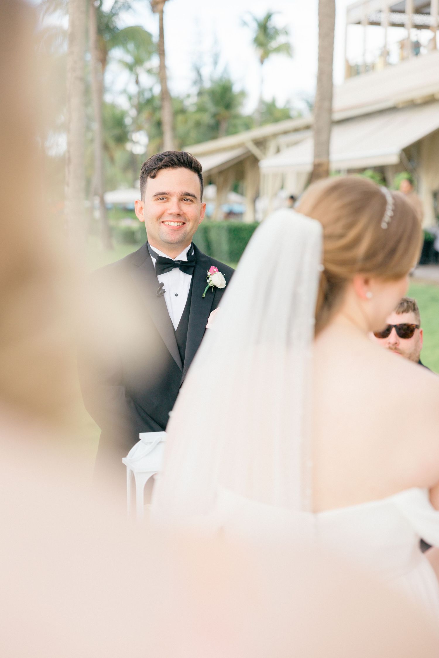 Candid moments captured during outdoor wedding ceremony with palm trees and building in background.